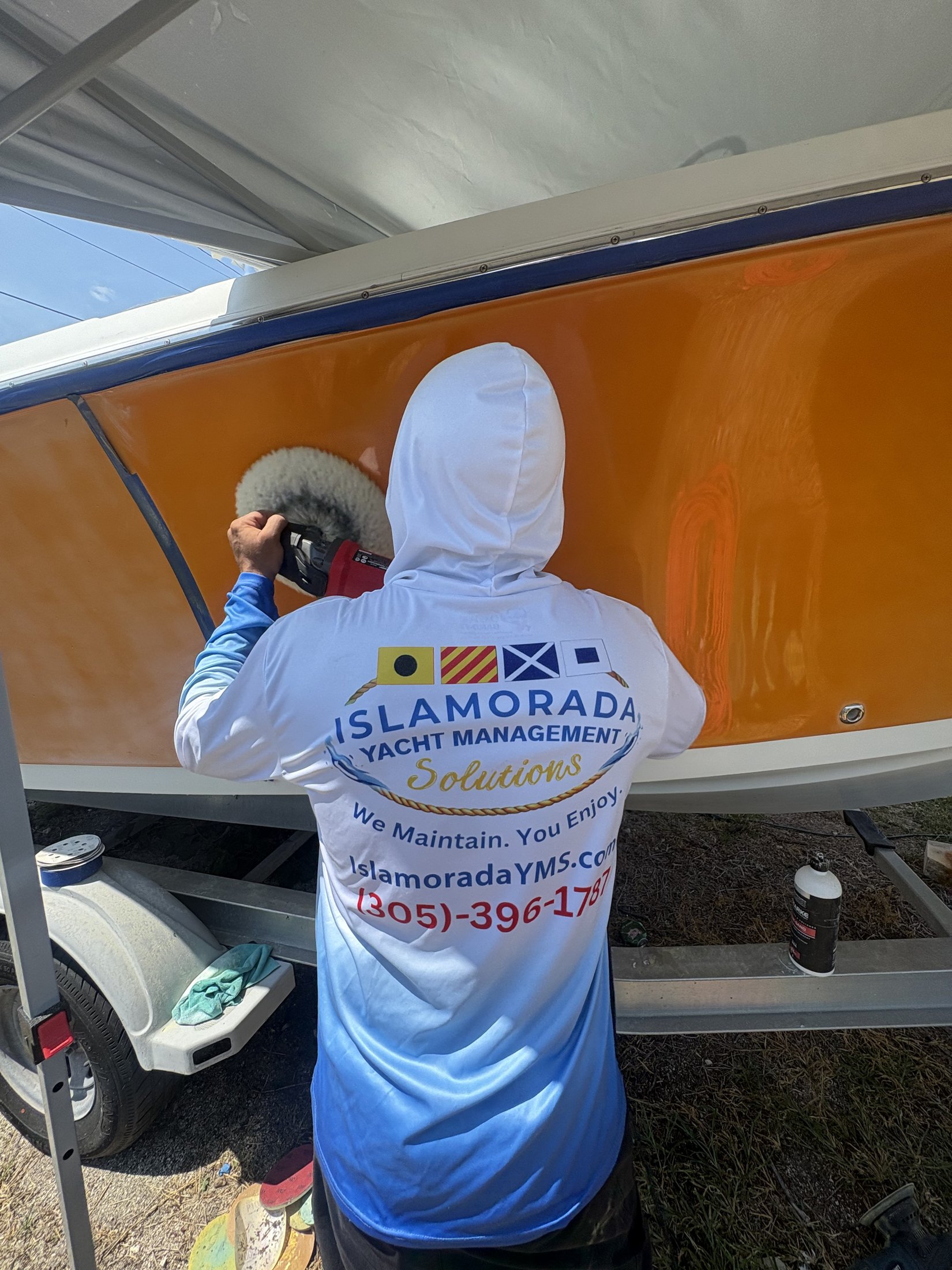 IYMS technician using a polisher on an orange yacht hull